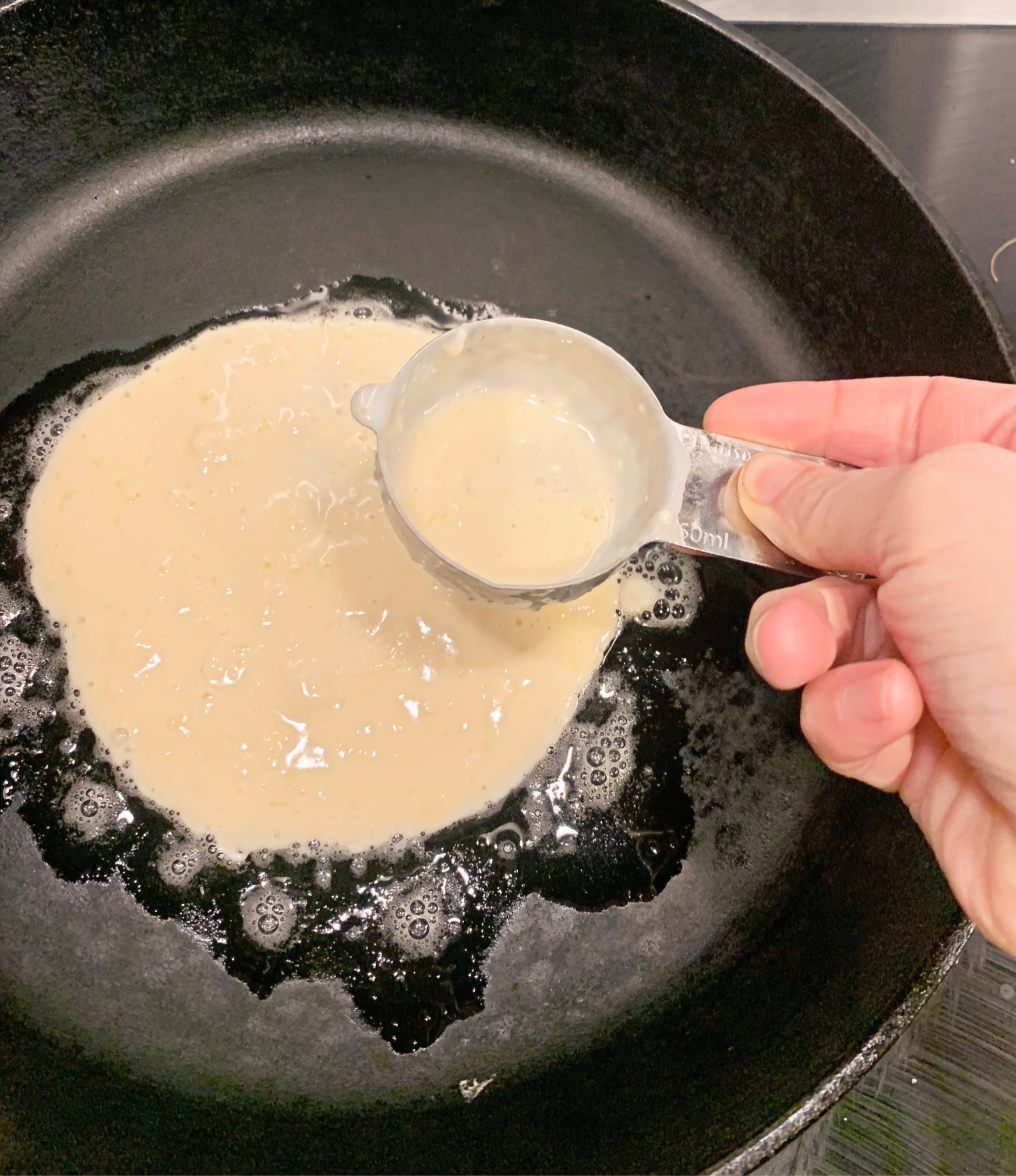 Spreading pancake batter with back of measuring cup