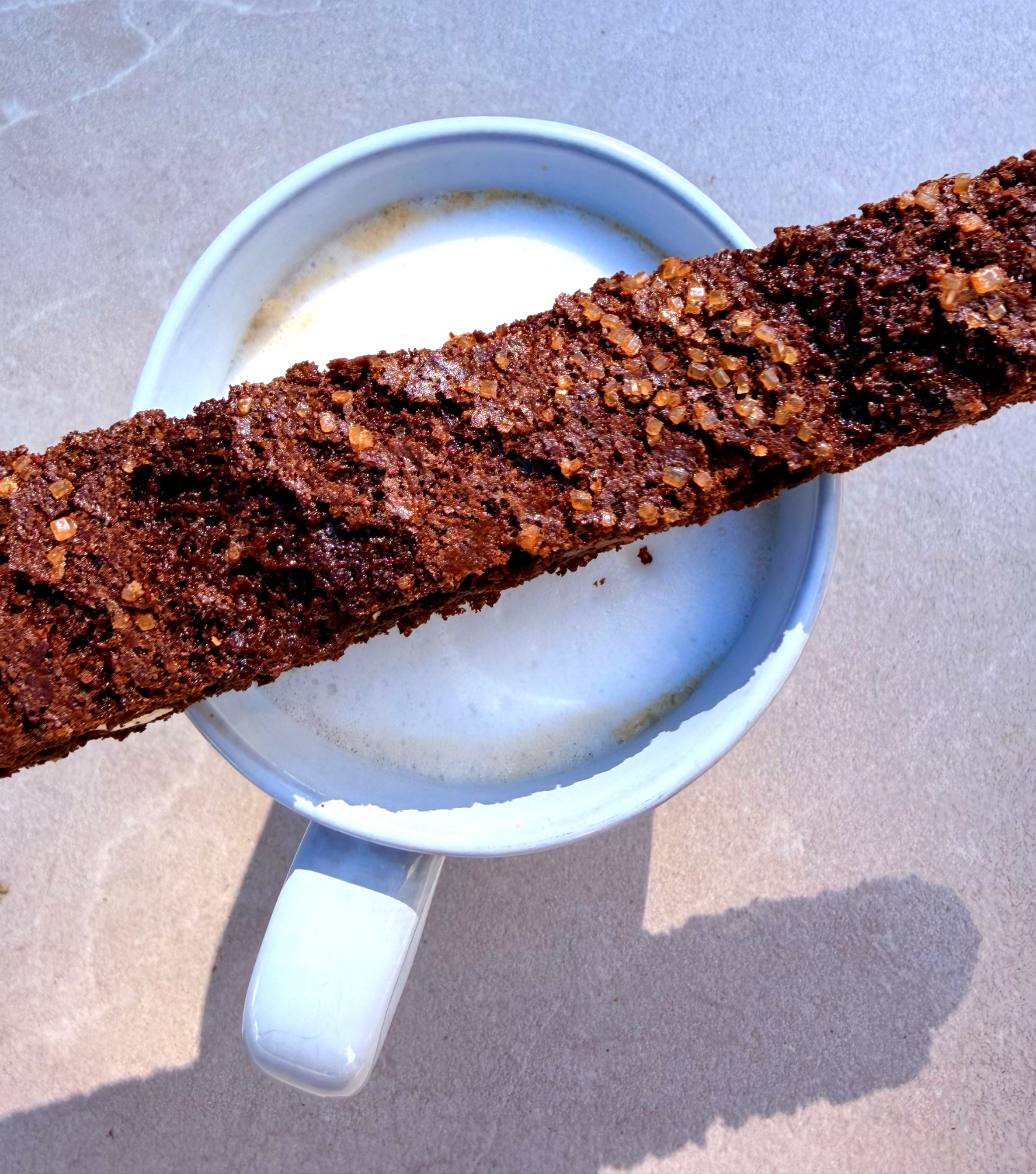 chocolate biscotti on top of cappuccino in a mug